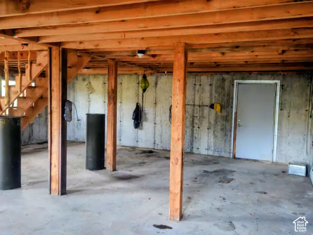 Finished basement area featuring concrete flooring, exposed wood beam ceiling, wood staircase, and concrete walls