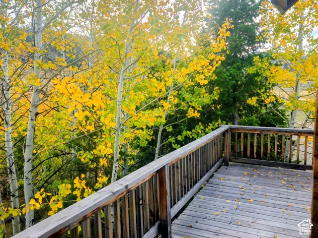 Expansive wooden deck with railing, surrounded by mature trees, featuring a log cabin wall