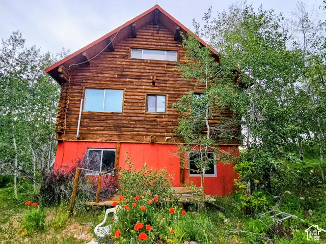 Log cabin exterior featuring a vibrant red lower level, multiple windows, and natural landscaping with mature trees and ground cover