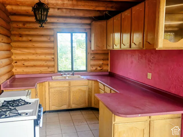 Log wall construction featuring wood-finish cabinetry, a window over the sink, and a built-in electric range