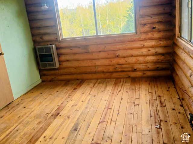 Wood-finish flooring, log wall construction, multiple windows, wall-mounted heater, and a wood-panel door