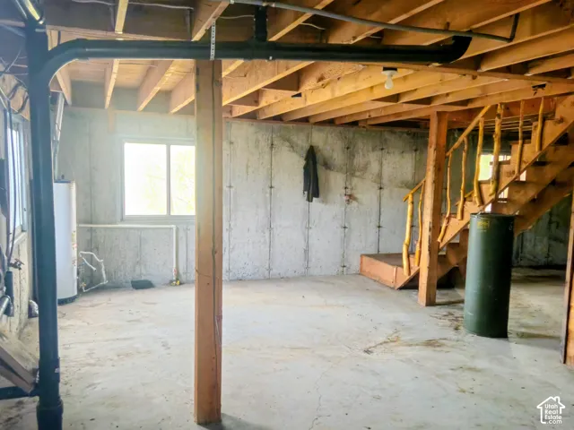 Exposed wood ceiling joists with visible plumbing, concrete flooring, and a wooden staircase