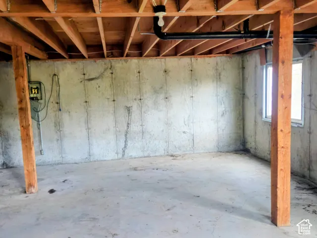 Unfinished basement featuring concrete walls, concrete flooring, exposed wood ceiling joists, and a window