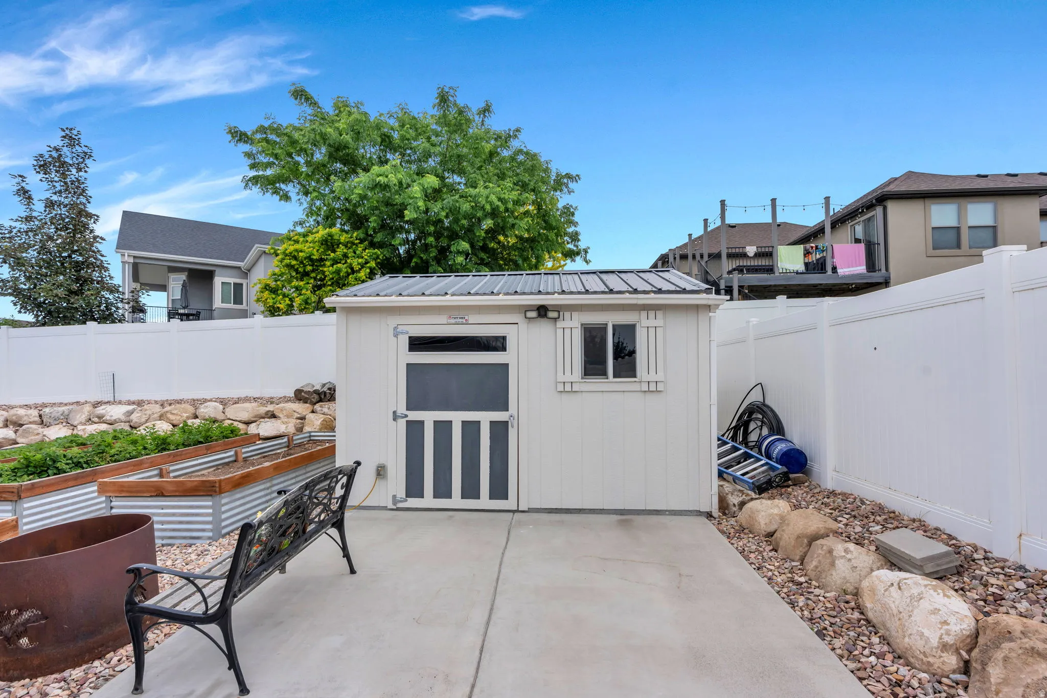 Backyard features a white utility shed with a metal roof, a concrete patio, and a white privacy fence