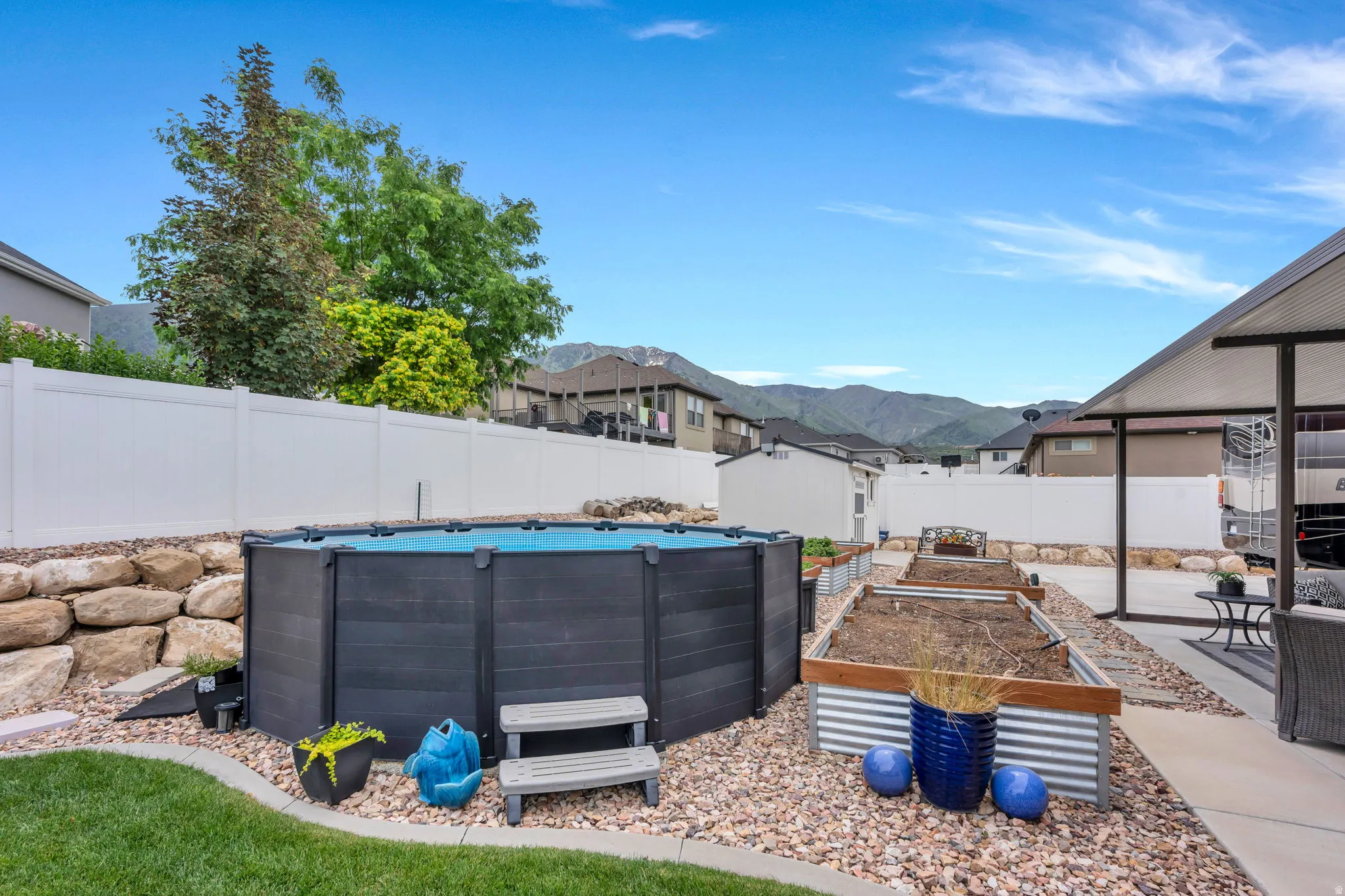 Backyard oasis featuring an above-ground swimming pool, multiple raised garden beds, a covered patio area, and a white privacy fence