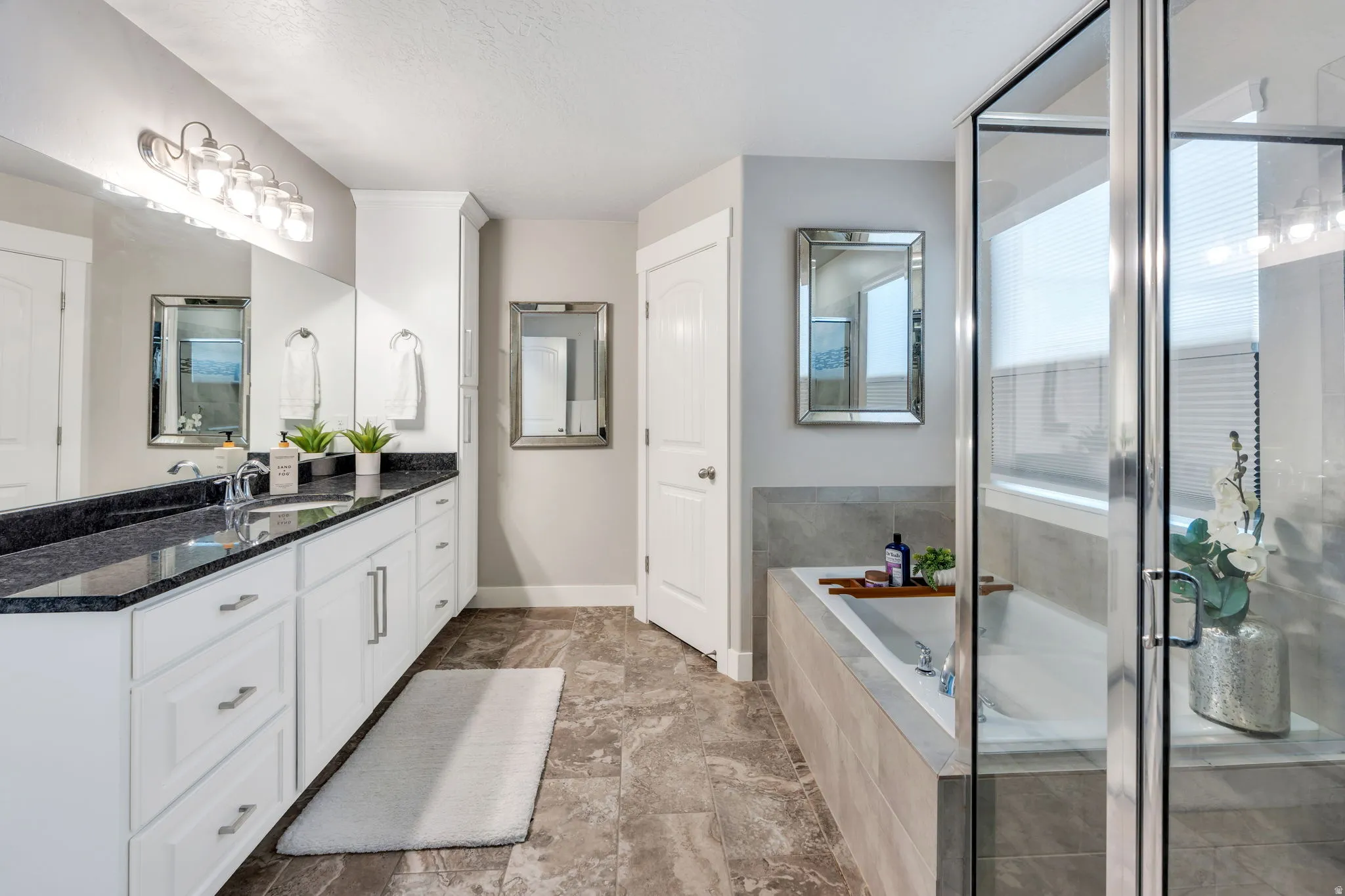 Spacious bathroom featuring a dual vanity with a dark countertop and white cabinetry, a large soaking tub, and a separate glass-enclosed shower