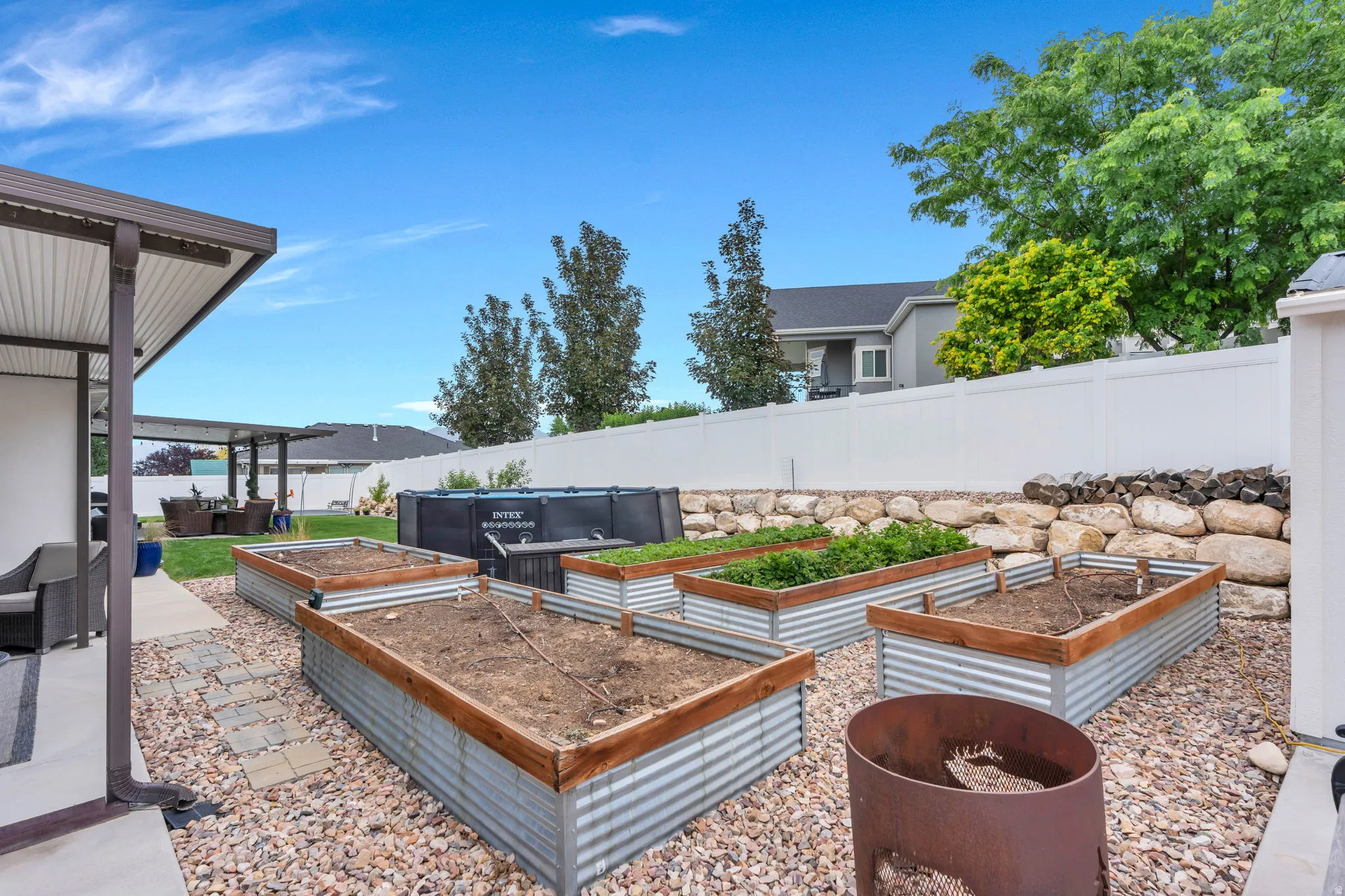 Expansive backyard featuring multiple corrugated metal raised garden beds with wood trim, a rock-lined retaining wall, and a large gravel area