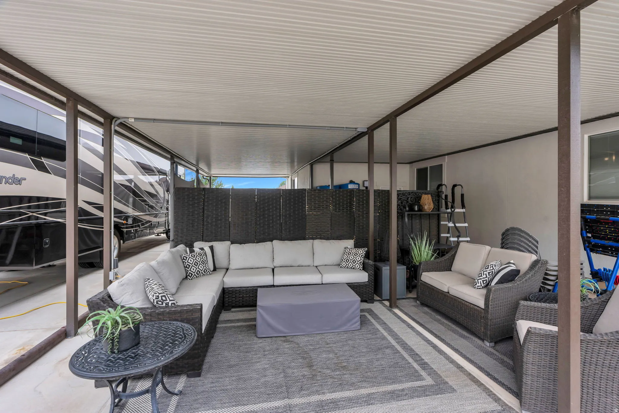 Covered patio area featuring a corrugated metal roof, support beams, and an exterior wall with a sliding window