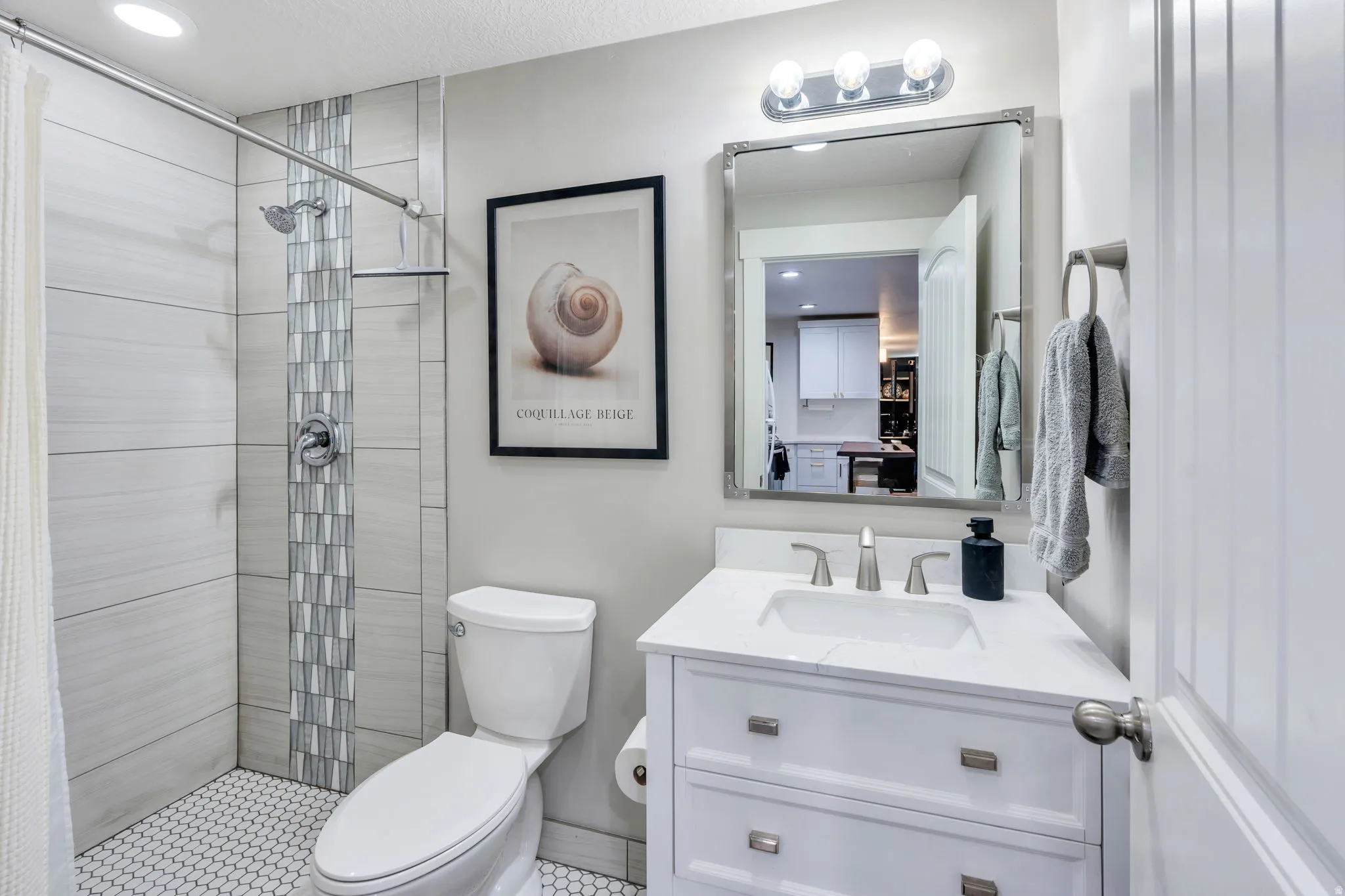 Bathroom featuring a tiled shower with mosaic accent, white tile flooring, and a vanity with an integrated sink and quartz countertop
