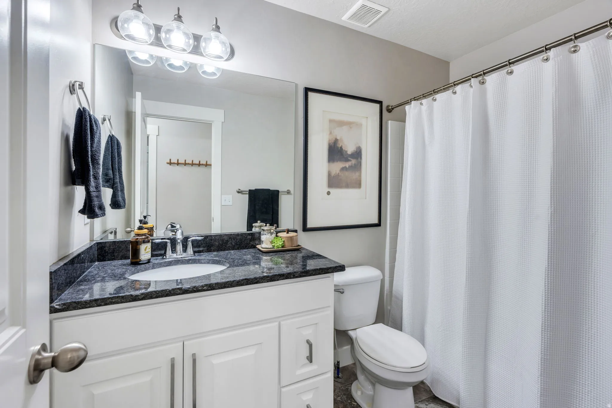 Bathroom featuring a white vanity with panel cabinetry, dark countertop, and an undermount sink
