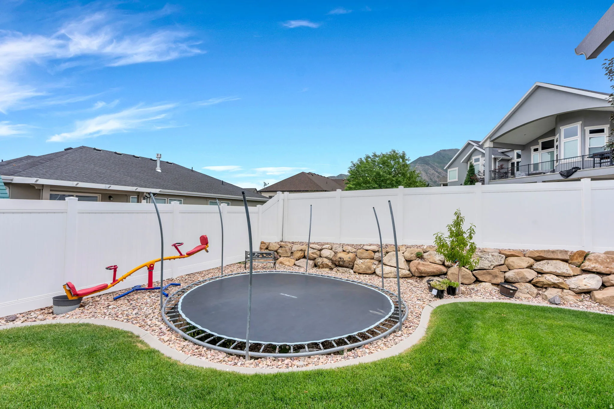 Expansive backyard featuring a manicured lawn, white vinyl fencing, and a stone retaining wall