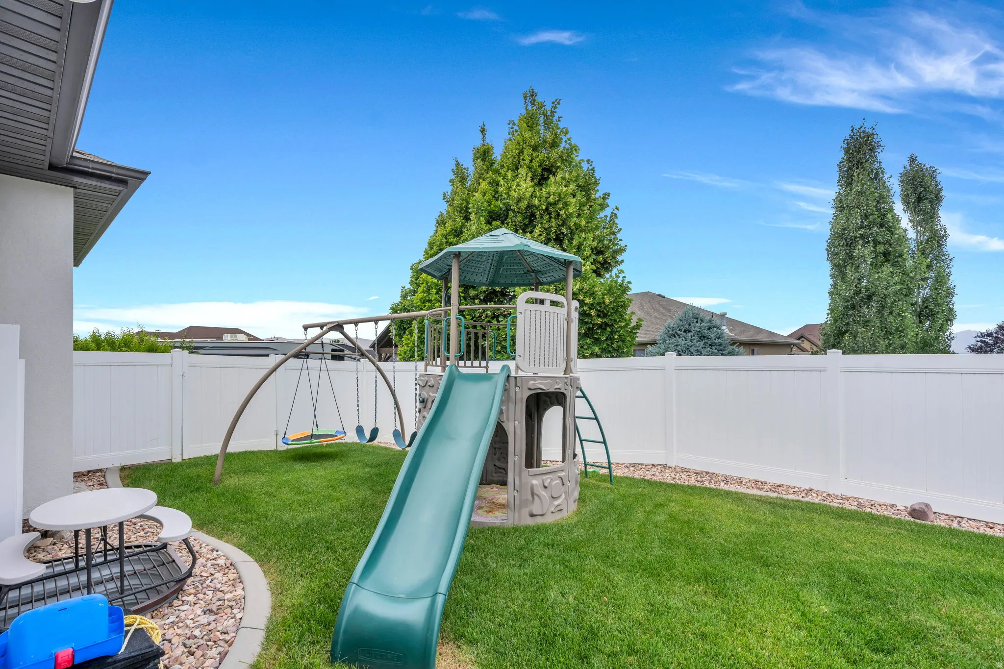 Enclosed backyard featuring a manicured lawn, white vinyl fencing, and a decorative rock border