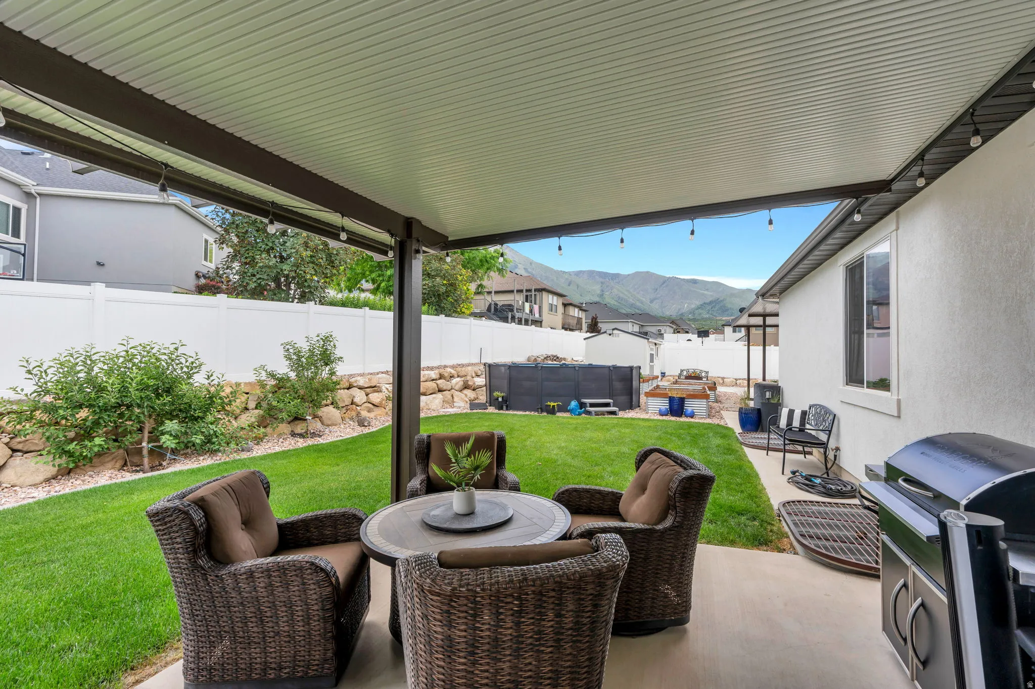 Covered patio overlooking a manicured lawn, rock retaining wall, and mountain scenery