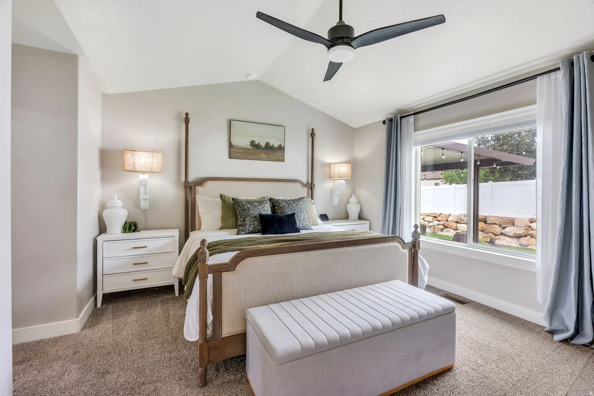 Master bedroom featuring a vaulted ceiling, ceiling fan, and large window with exterior rock landscaping