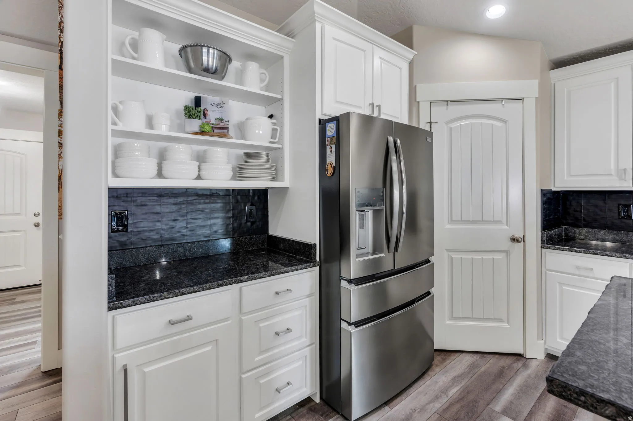 Kitchen featuring white shaker-style cabinetry, dark granite countertops, and a beautiful black subway tile backsplash