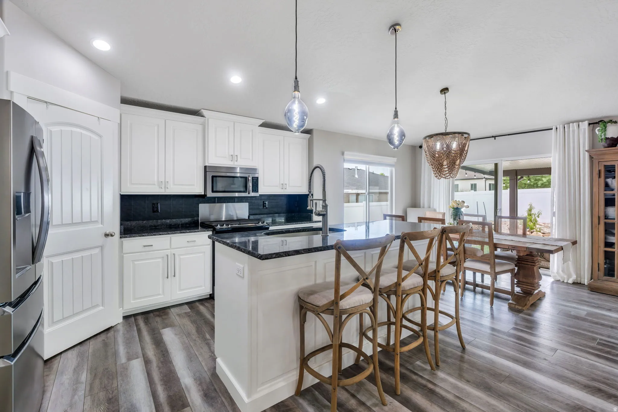 Kitchen with white cabinetry, dark countertops, wood-finish flooring, stainless steel appliances, and island seating