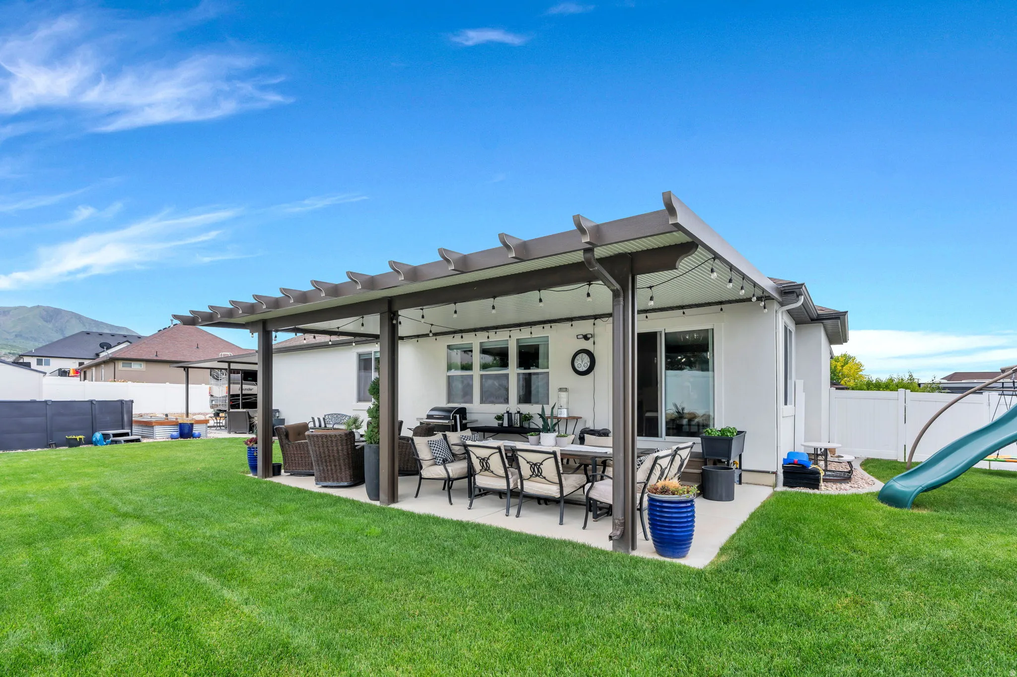 Expansive backyard featuring a covered patio with a large manicured lawn, a sliding glass door, and a white privacy fence