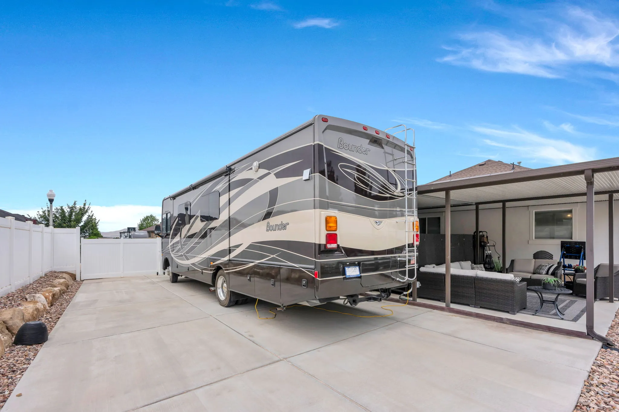 Concrete RV parking pad with gated access, white vinyl fencing, and a covered patio area