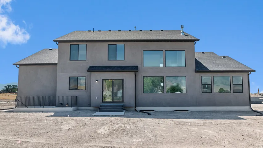 Contemporary stucco exterior featuring a tiered roofline, expansive window array, black-framed sliding glass door, and a ground-level concrete patio with a black metal railing