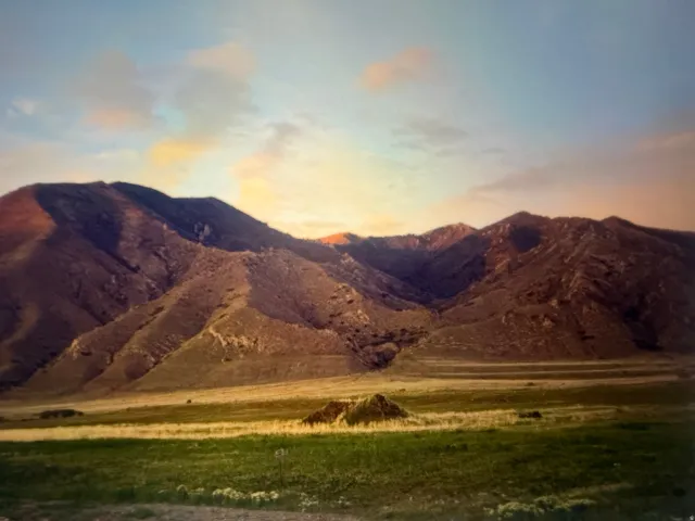 Expansive mountain range backdrop with natural terrain and a broad field of green and gold grasses in the foreground