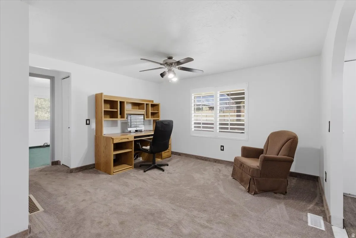 Carpeted room with white walls, a ceiling fan with light fixture, and a window with white plantation shutters