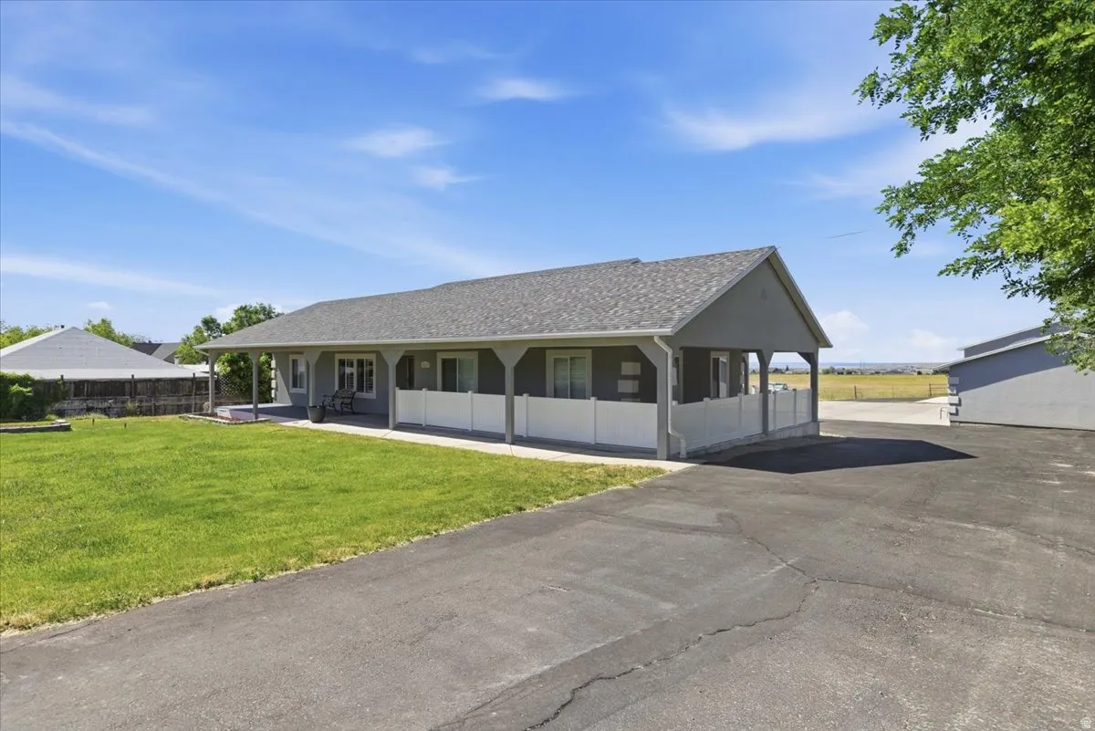 Ranch-style exterior with a covered front porch, asphalt driveway, and a spacious green lawn