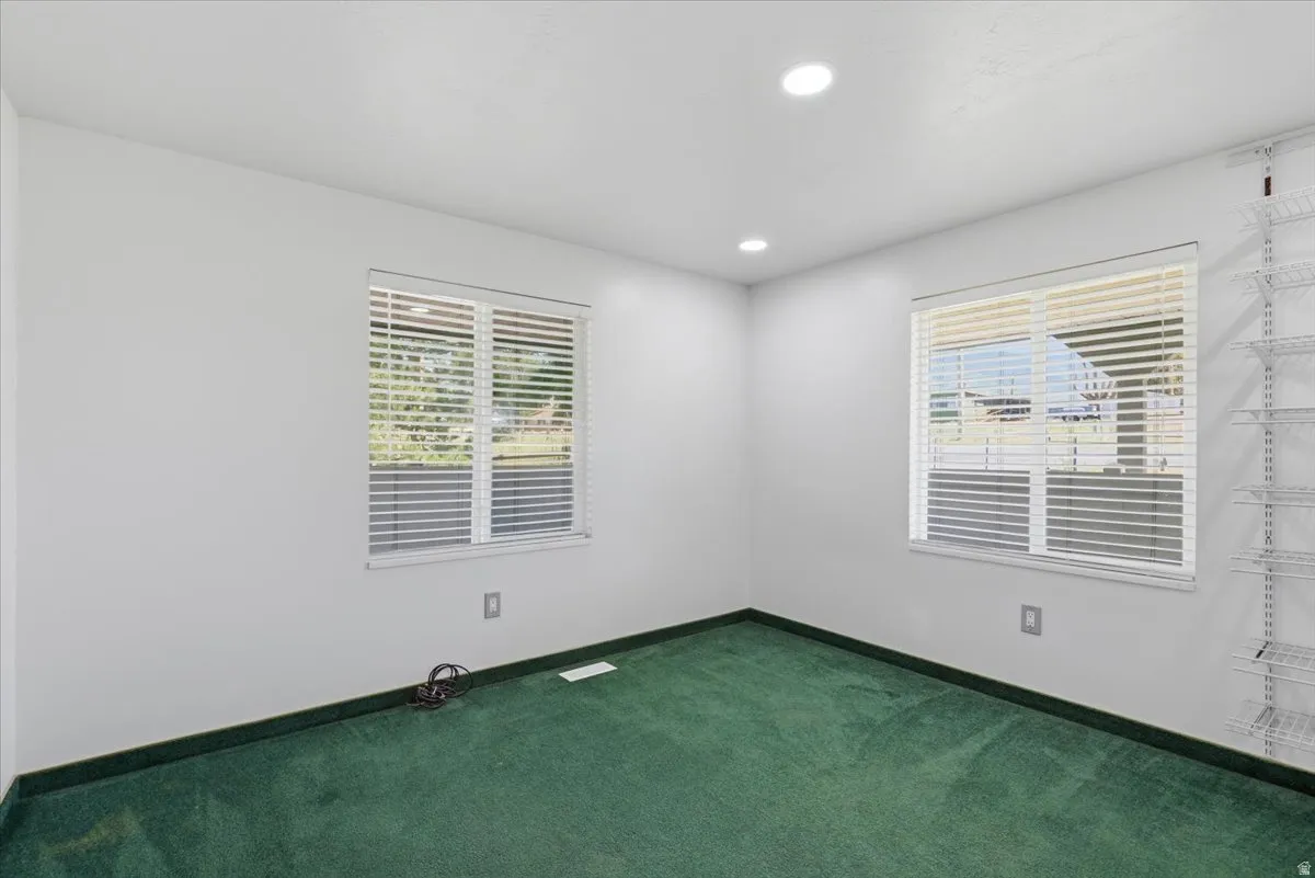 Bright interior room featuring two windows with horizontal blinds, recessed lighting, white walls, and green carpeting