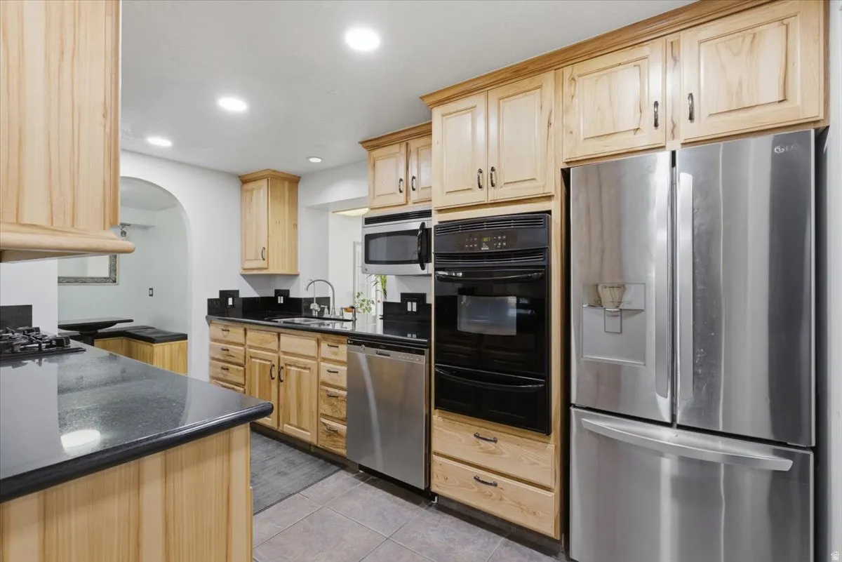 Kitchen featuring light wood cabinetry, dark countertops, integrated stainless steel appliances, and recessed lighting
