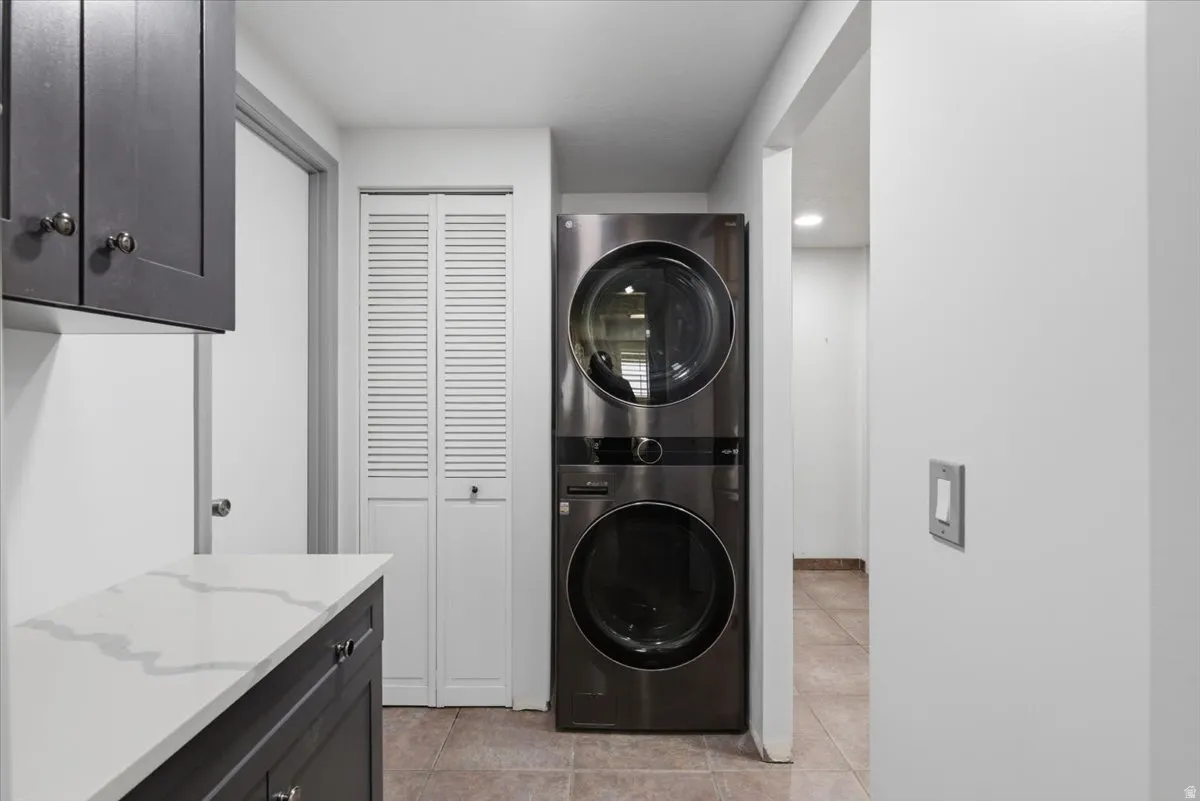Dedicated laundry area featuring a stacked washer and dryer, dark wood-finish cabinetry, and a white countertop with grey veining