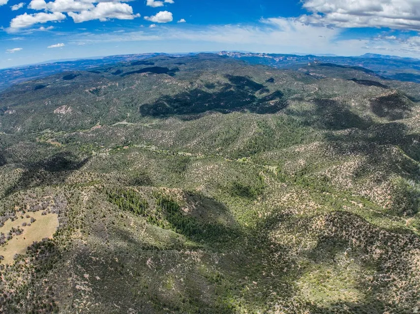 Expansive mountainous terrain featuring diverse vegetation, rolling hills, and a clear blue sky with scattered clouds
