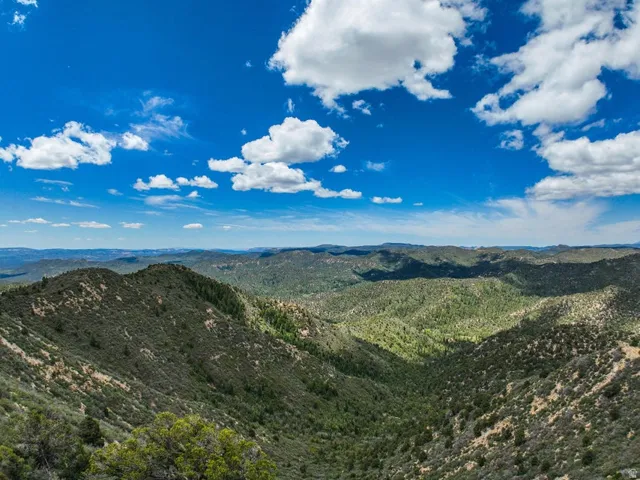 Expansive mountainous landscape featuring distant green hills under a bright blue sky with scattered clouds