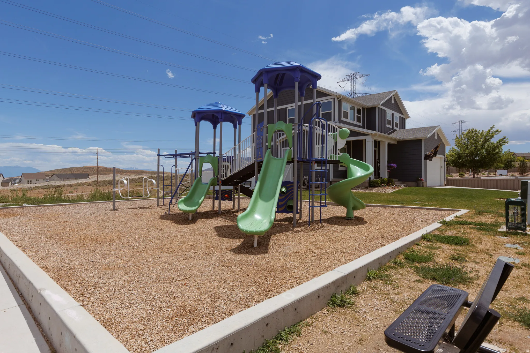 Community playground featuring multiple slides, climbing elements, wood chip surfacing, and dedicated open-air fitness equipment
