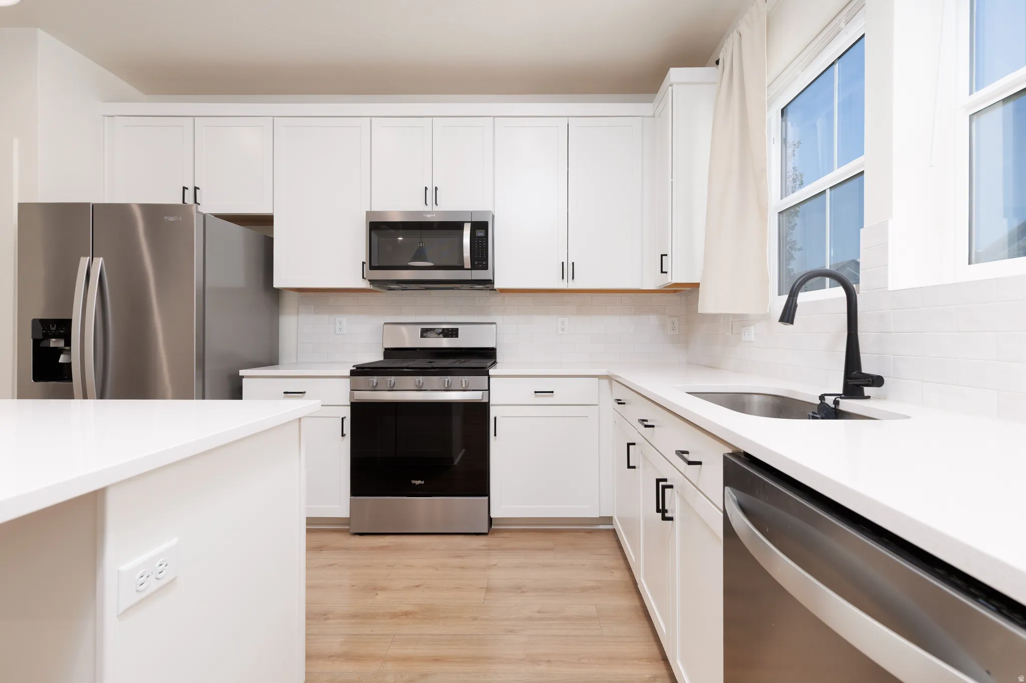 Modern kitchen featuring white cabinetry, stainless steel appliances, a white subway tile backsplash, and light wood-finish flooring