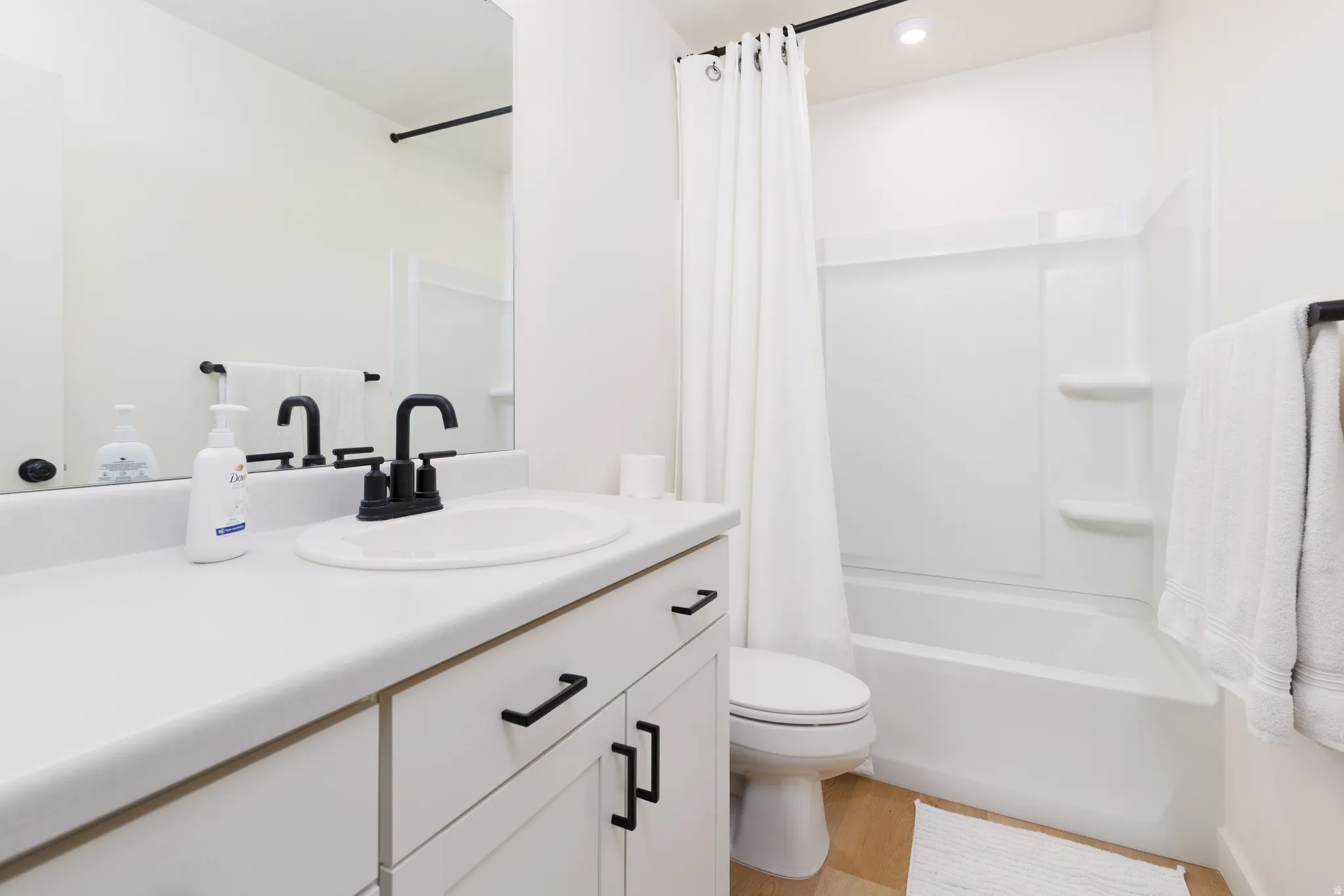 Contemporary bathroom featuring a white vanity with black hardware, a black faucet, a white tub-shower combination, and wood-finish flooring