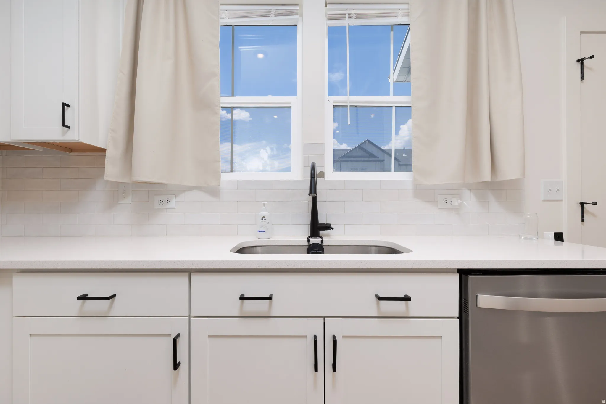 Kitchen sink with a matte black faucet, white shaker-style cabinetry, and a subway tile backsplash
