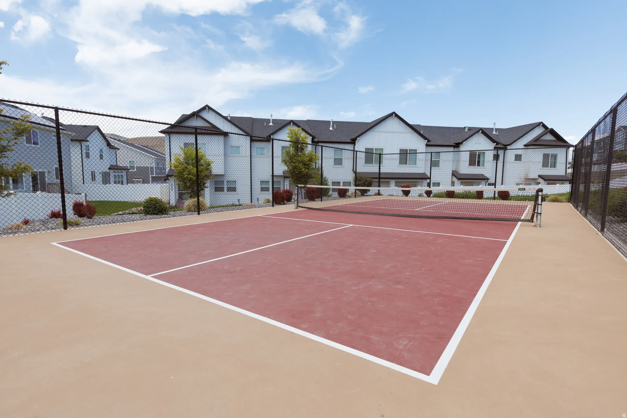 Tennis court with a red playing surface, white boundary lines, and a dark net