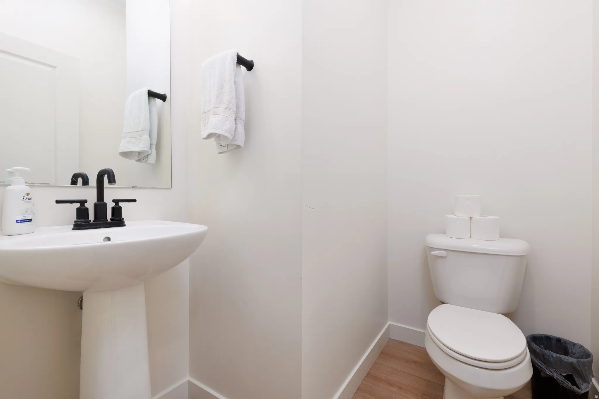 Pedestal sink featuring a matte black faucet, mirrored wall, and wood-finish flooring