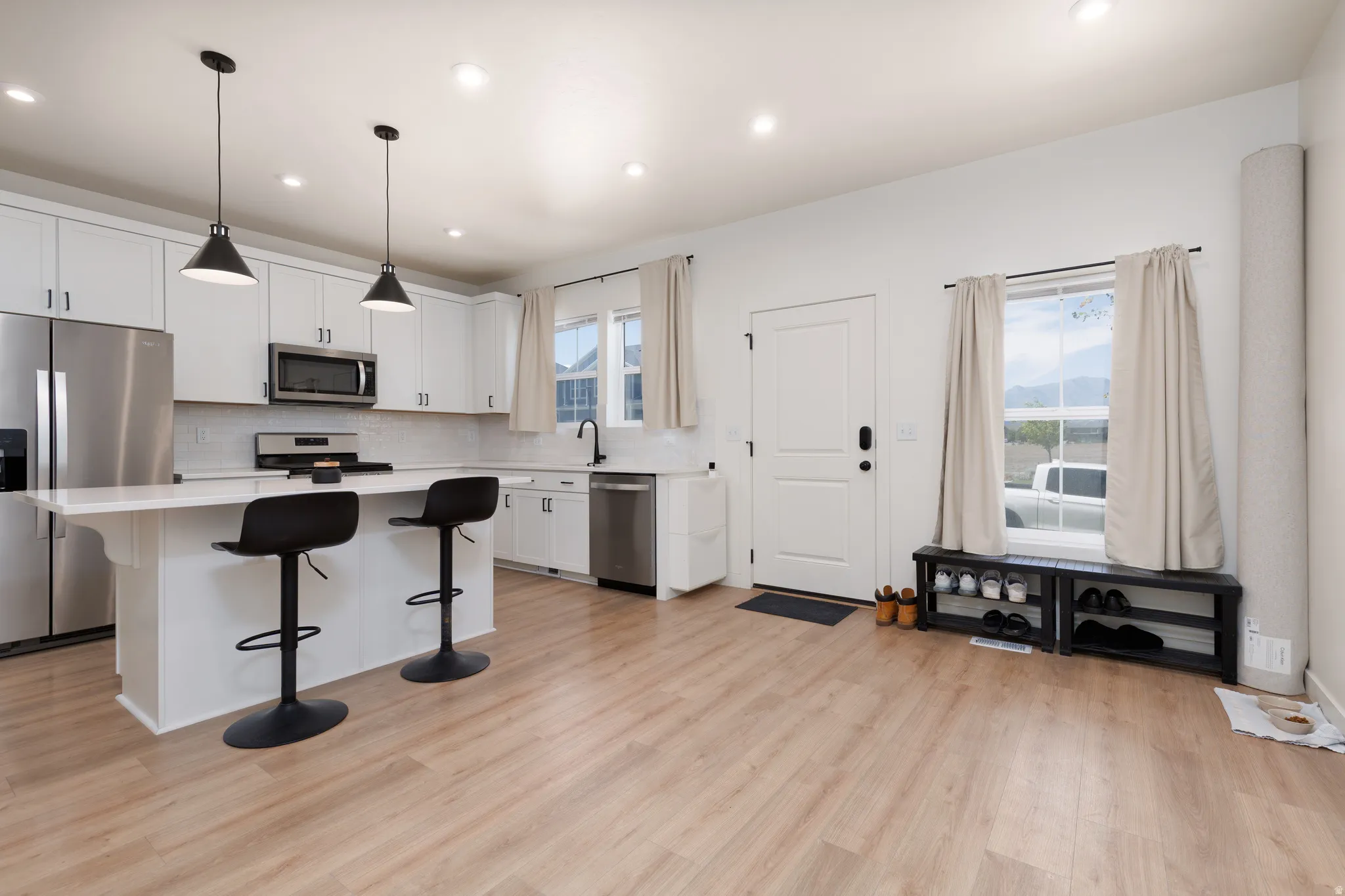 Open-concept kitchen featuring white cabinetry, stainless steel appliances, a white subway tile backsplash, and light wood-finish flooring