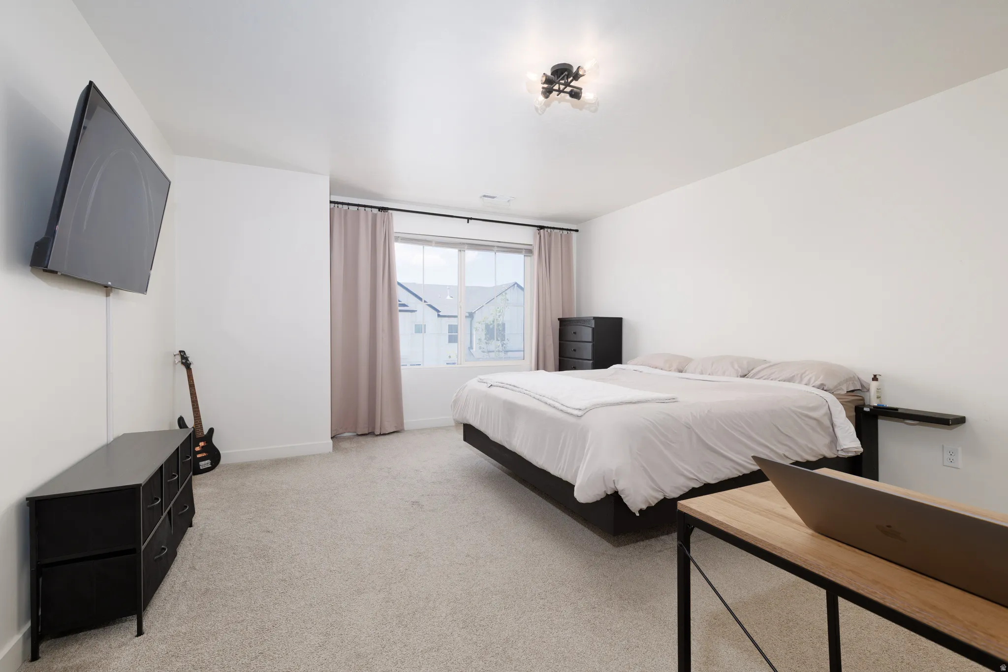 Carpeted bedroom featuring white walls, a large window with privacy curtains, and a contemporary ceiling light fixture