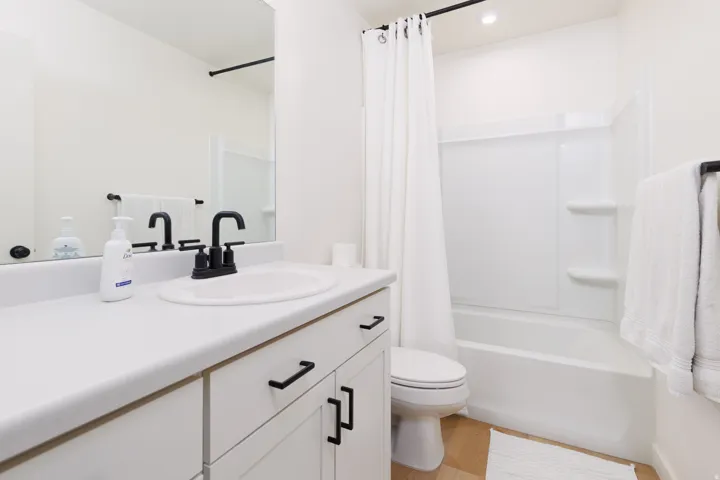 Contemporary bathroom featuring a white vanity with black hardware, a black faucet, a white tub-shower combination, and wood-finish flooring