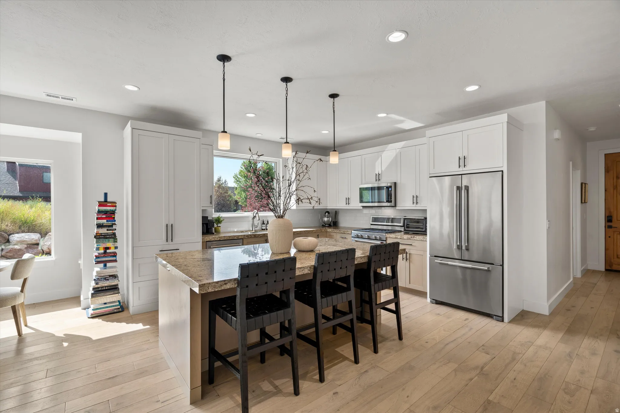Kitchen featuring light wood-finish flooring, white cabinetry, stainless steel appliances, and a granite countertop island with seating.