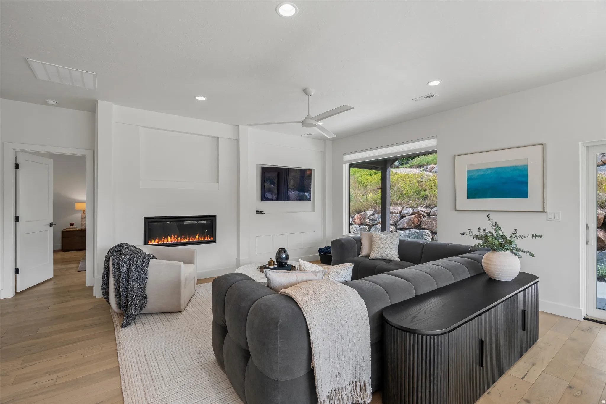 Spacious living area featuring light wood-finish flooring, recessed lighting, and a modern linear fireplace.