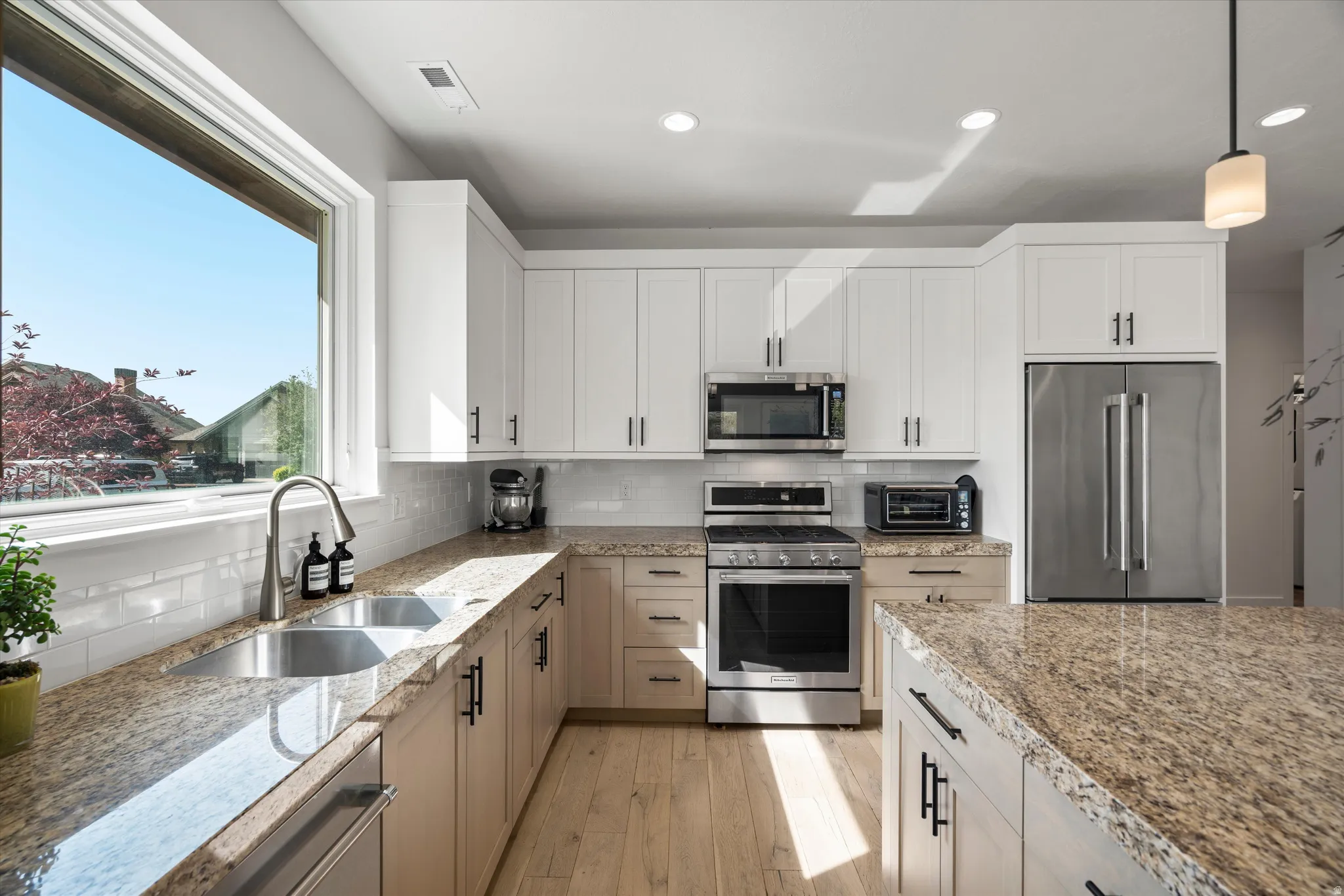 Kitchen featuring wood-finish flooring, two-tone cabinetry with matte black hardware, stainless steel appliances, a subway tile backsplash, and stone countertops.