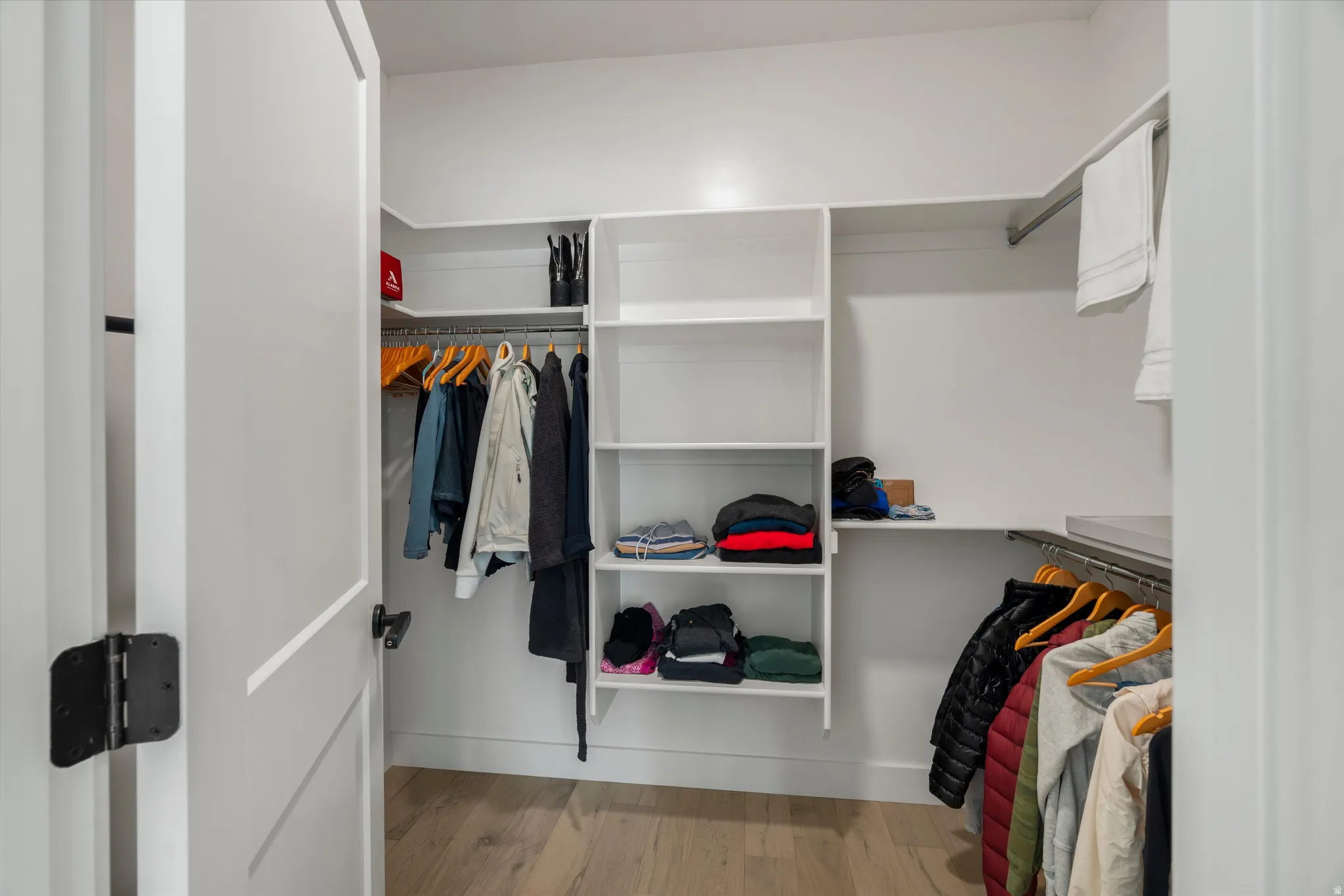 Primary suite walk-in closet system featuring multiple shelves, hanging rods, and light wood-finish flooring