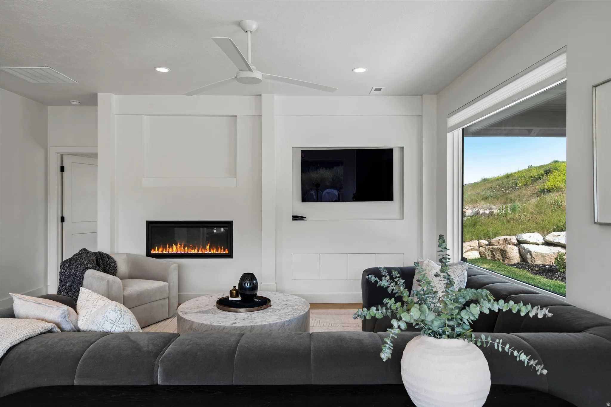 Living space featuring a built-in fireplace, a ceiling fan, recessed lighting, a large window, and built-in cabinetry.