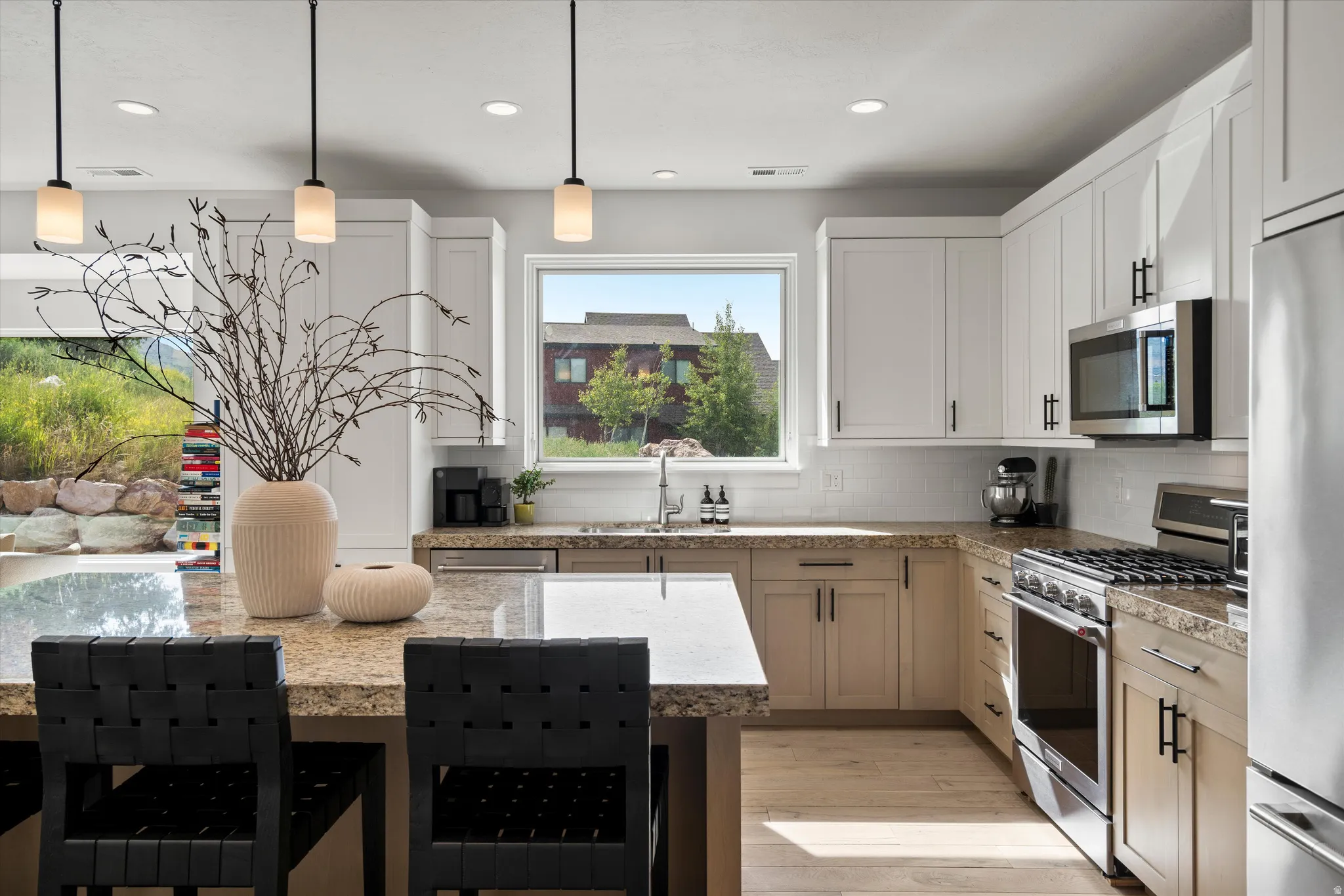 Spacious kitchen featuring a large island with a granite countertop, light wood-finish flooring, white upper cabinetry, and stainless steel appliances.