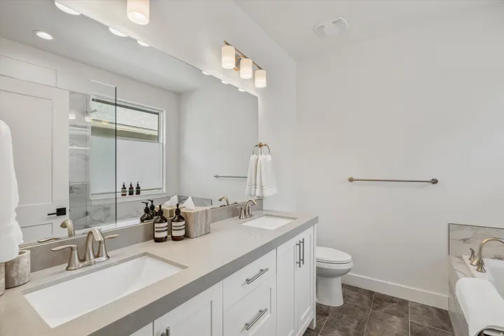 Bathroom featuring a double vanity with light gray countertops and undermount sinks, white cabinetry with brushed nickel hardware, and a large mirror with integrated lighting
