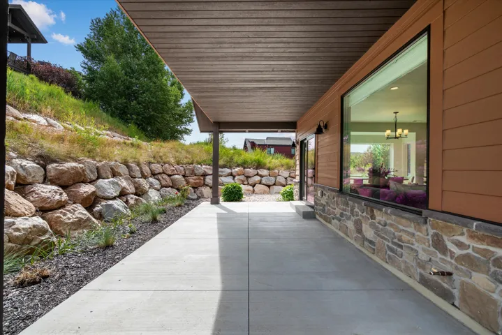 Covered concrete patio with wood-finish ceiling, flanked by a stacked stone retaining wall and a horizontal plank exterior.