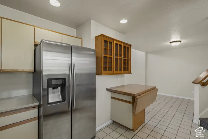 Kitchen area featuring a stainless steel side-by-side refrigerator, cream-colored upper and lower cabinetry, and a wood-finish drop-leaf counter
