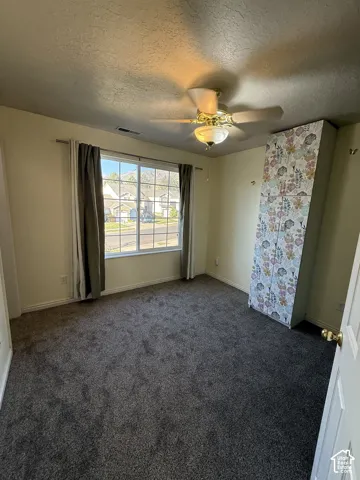 Wall-to-wall carpeting in a neutral tone, ceiling fan with integrated lighting, and a large window providing natural illumination